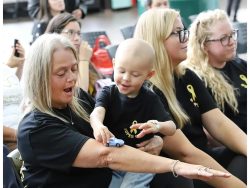 A volunteer holds a child while they play with a toy car at a community event.
